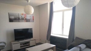 Una sala de estar moderna con un televisor de pantalla plana, un sofá, una mesa de centro y un ventanal con cortinas.