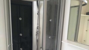 Una ducha en esquina con puerta de vidrio, un lavamanos blanco con un espejo arriba y un dispensador de jabón morado.