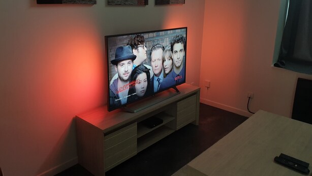 Un televisor sobre un soporte de madera y un control remoto sobre una mesa al frente.