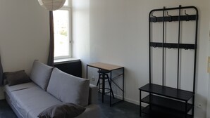 Una sala de estar minimalista con un sofá gris, una mesita de madera pequeña y una estantería de metal negro.