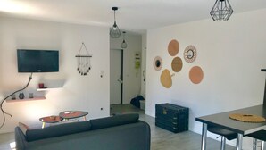 A modern living room with a grey sofa, a TV mounted on the wall, a dining area with a table and chairs, and decorative wall art. - The Central (beautiful apartment in a quiet hyper-center) (Nancy)