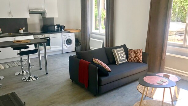 A modern living space with a sofa, a dining table, a kitchen area, and a laundry machine. - The Central (beautiful apartment in a quiet hyper-center) (Nancy)