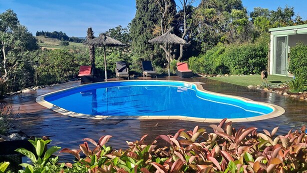 A swimming pool with a wooden deck, surrounded by lush greenery and trees. - CHAMBRE D'HOTE MERLOT CHEZ LE VIGNERON (LAURE MINERVOIS)