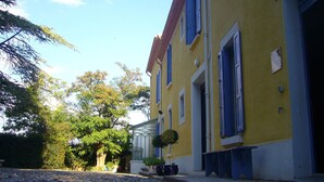 A yellow building with blue shutters and a stone pathway leading to it. - CHAMBRE D'HOTE MERLOT CHEZ LE VIGNERON (LAURE MINERVOIS)