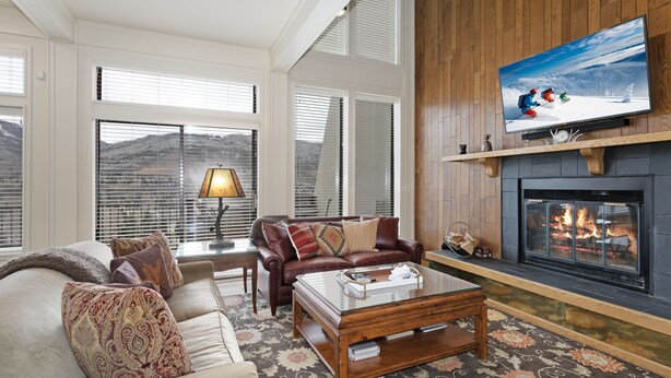 A living room with a fireplace, a sofa, a coffee table, and a television mounted on the wall. - 15 Chambertin Townhomes  3 Bedroom Townhouse by RedAwning (Avon)