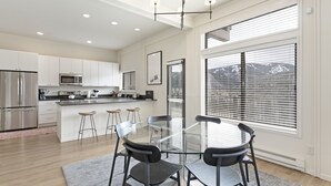 A modern kitchen with stainless steel appliances, a glass dining table with chairs, and large windows with blinds. - 15 Chambertin Townhomes  3 Bedroom Townhouse by RedAwning (Avon)