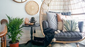 A wicker chair with cushions, a potted plant, and a small table with a bowl and stones.