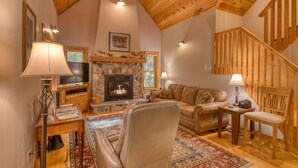 Una sala de estar acogedora con chimenea de piedra, techo de madera y una escalera.