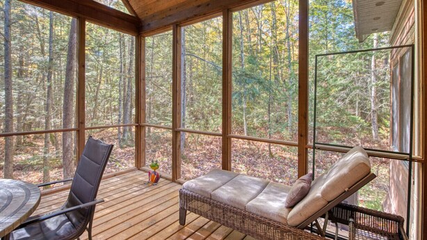 Una terraza de madera con una silla lounge de mimbre y una mesa, con vista a un bosque.