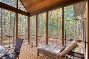 Una terraza de madera con una silla lounge de mimbre y una mesa, con vista a un bosque.