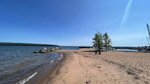 Una playa con cielo despejado, orilla arenosa, un árbol y un muelle con barcos.