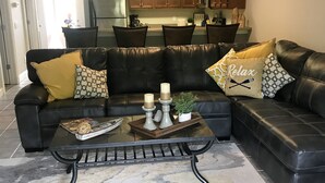 Ein modernes Wohnzimmer mit einem schwarzen Leder-Sofa, einem Couchtisch und einer Küche im Hintergrund.
