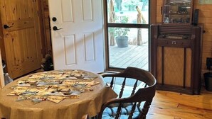 Ein Blockhaus-Interieur mit einem runden Tisch, Holzstühlen, einer zur Außenwelt führenden Tür und einem Holzschrank mit einem Radio.