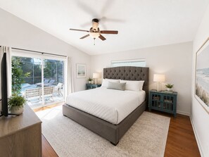 A bedroom with a large bed, a ceiling fan, a sliding glass door to a patio, and a small nightstand with a lamp. - Beach Retreat 4BR, Spa, Heated Pool, Screened Lanai (St. Augustine)