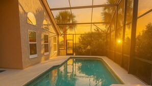 A swimming pool with a view of a sunset, surrounded by a covered area with glass walls. - Summer Pool Retreat Near Vilano Beach (St. Augustine)