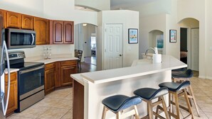 A modern kitchen with wooden cabinets, a stainless steel stove, a microwave, and a large island with bar stools. - Summer Pool Retreat Near Vilano Beach (St. Augustine)