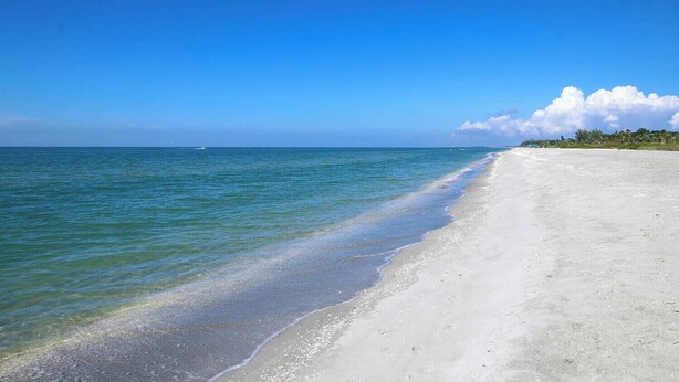 A beach with clear blue water, a sandy shore, and a distant shoreline with vegetation. - 3BR Captiva Village Retreat with Private Pool & Spa, Steps to the Beach (Captiva)
