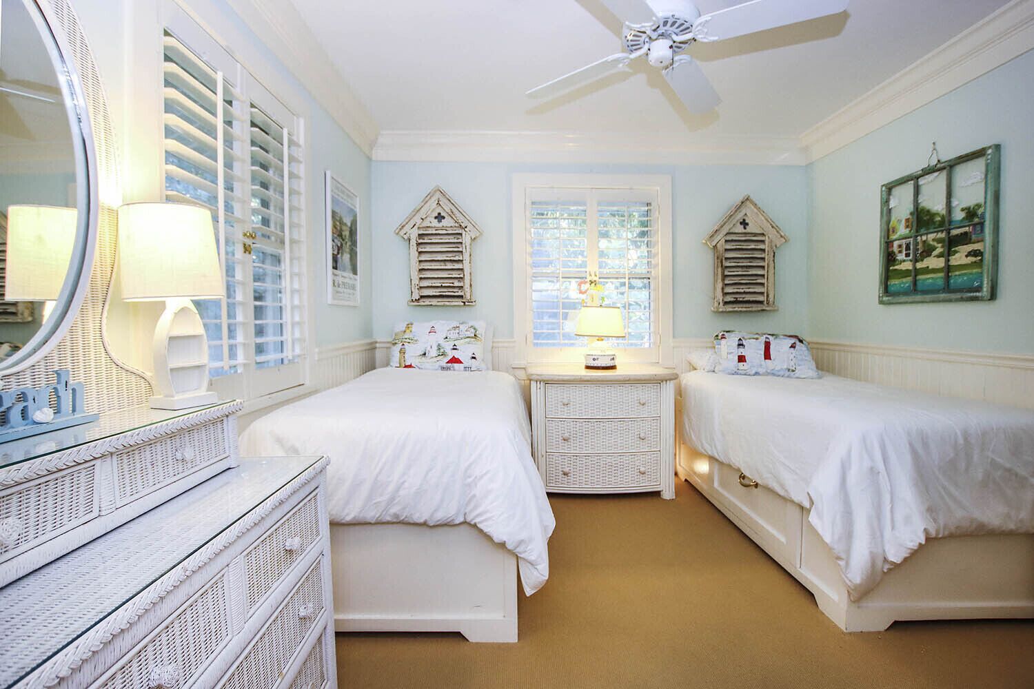 A bedroom with two beds, a dresser, a mirror, a ceiling fan, and a window with shutters.