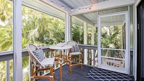 A covered outdoor area with wicker furniture, a small table, and a view of greenery.