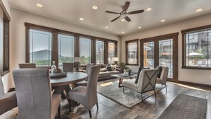 A spacious living room with a dining area, large windows, and a ceiling fan. - Luxe Townhome in Prime Location, Private Hot Tub, Chef (Park City)