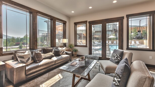 A spacious living room with large windows, a leather sofa, a coffee table, and a view of a pool and mountains. - Luxe Townhome in Prime Location, Private Hot Tub, Chef (Park City)