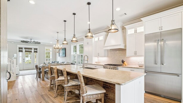 Une cuisine spacieuse dotée d’un grand îlot central, de meubles blancs, d’appareils électroménagers en acier inoxydable et de luminaires suspendus.