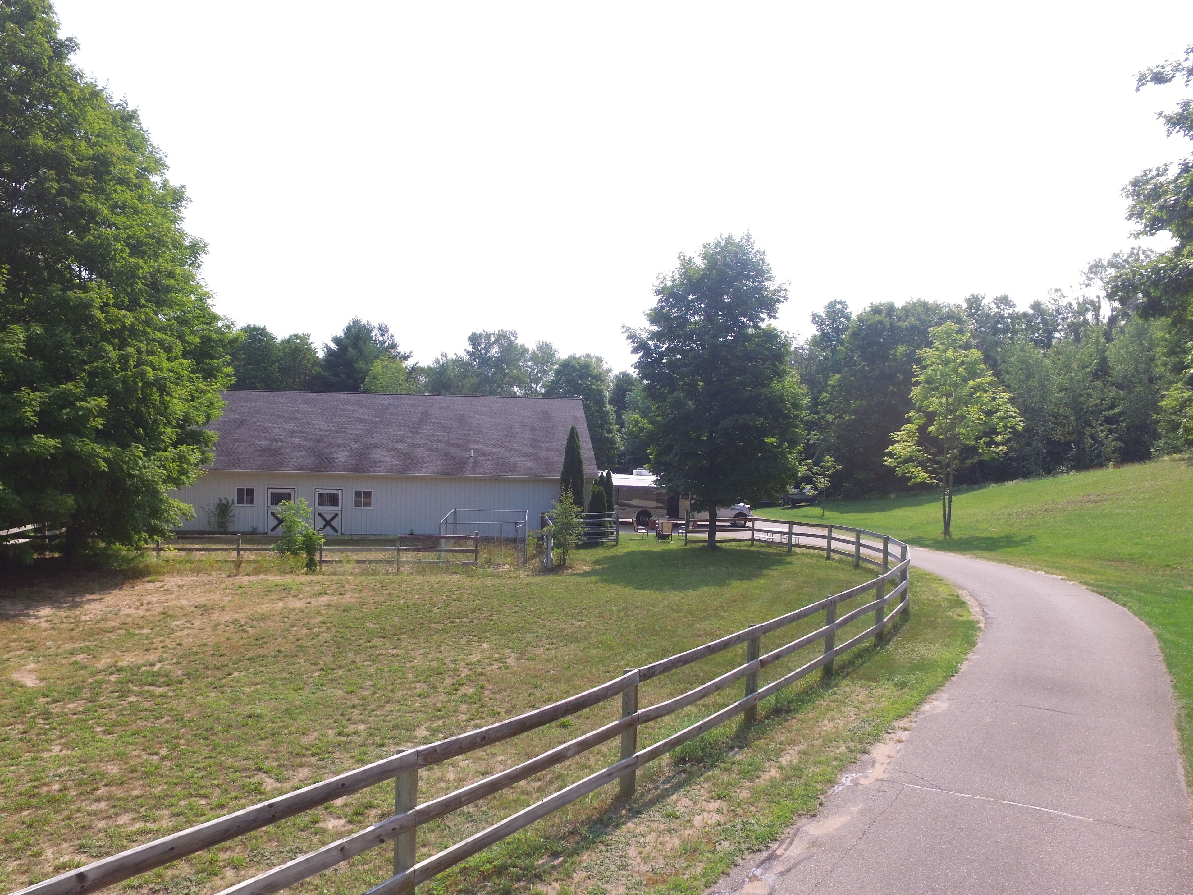 A rural property with a white barn, a fenced paddock, and a paved road curving through the landscape.