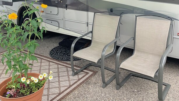 A recreational vehicle with a covered patio area, a small table, and two chairs.