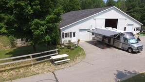 A white RV parked in front of a white building with a garage, a picnic table, and a bench.
