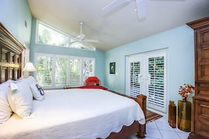 Une chambre dotée d’un grand lit, d’un ventilateur de plafond et offrant une vue sur l’extérieur par les fenêtres.