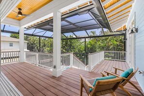 Um deck coberto ao ar livre com piso de madeira, guarda-corpos brancos e móveis de vime.