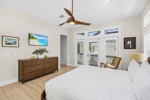 Ein Schlafzimmer mit einem Bett, einem Deckenventilator, einem Schminktisch, einem Fernseher und einem Fenster mit Jalousien.