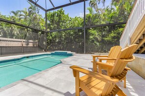 Ein Poolbereich mit Glasveranda, Holzliegen und Blick auf üppiges Grün.