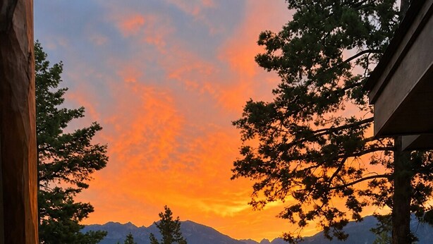 Eine Holzdar Terrasse mit Geländer, die auf einen See und die Berge bei Sonnenuntergang blickt.