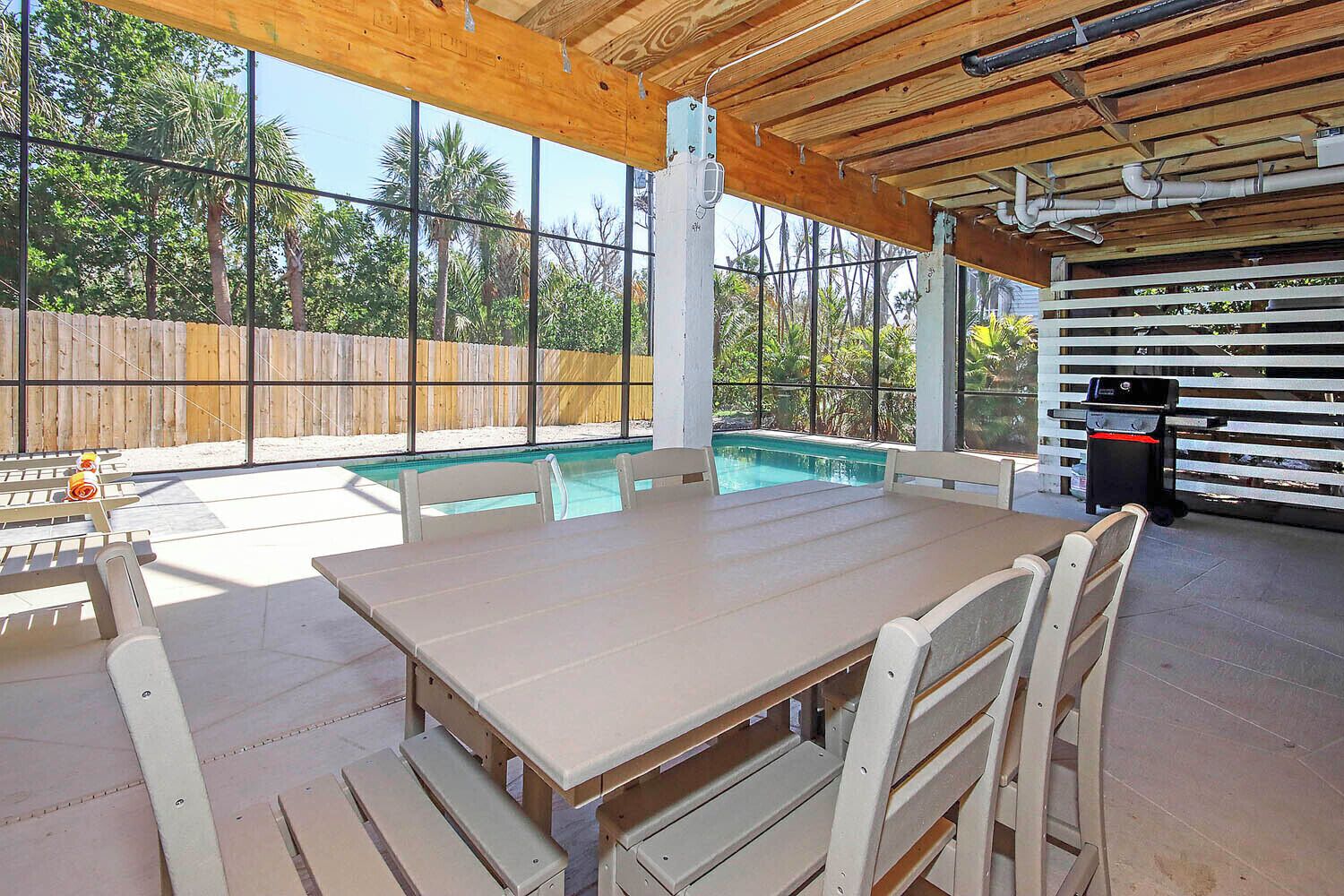 An outdoor patio with a pool, wooden tables and benches, and a barbecue grill.