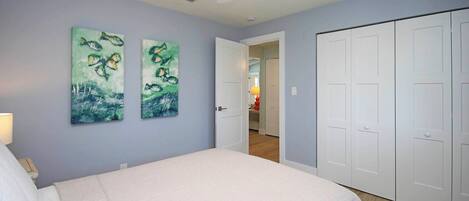 A bedroom with a bed, two paintings, a ceiling fan, and a set of white doors.