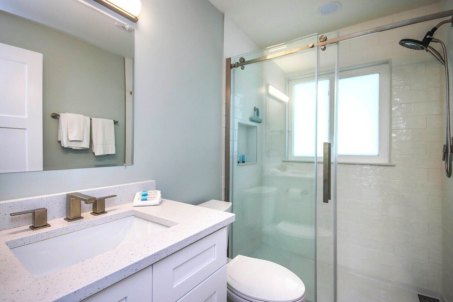 A modern bathroom with a glass-enclosed shower, a white sink with a single faucet, and a toilet.