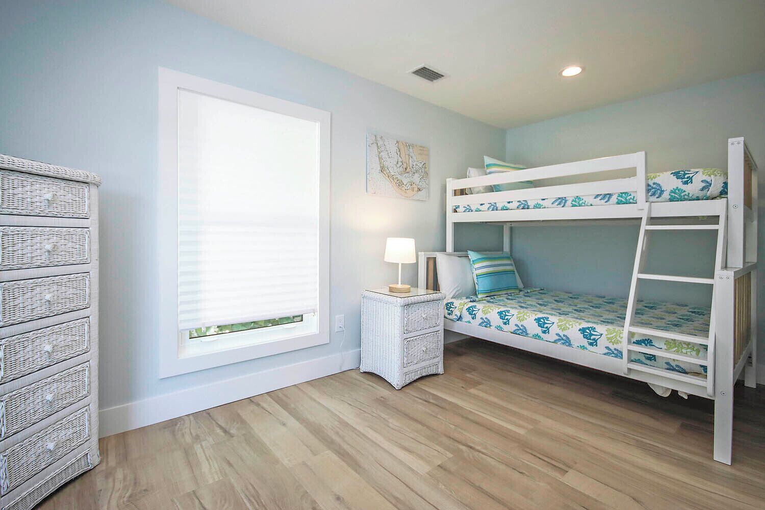 A child's bunk bed with a patterned bedspread, a small white side table with a lamp, and wicker baskets against the wall.