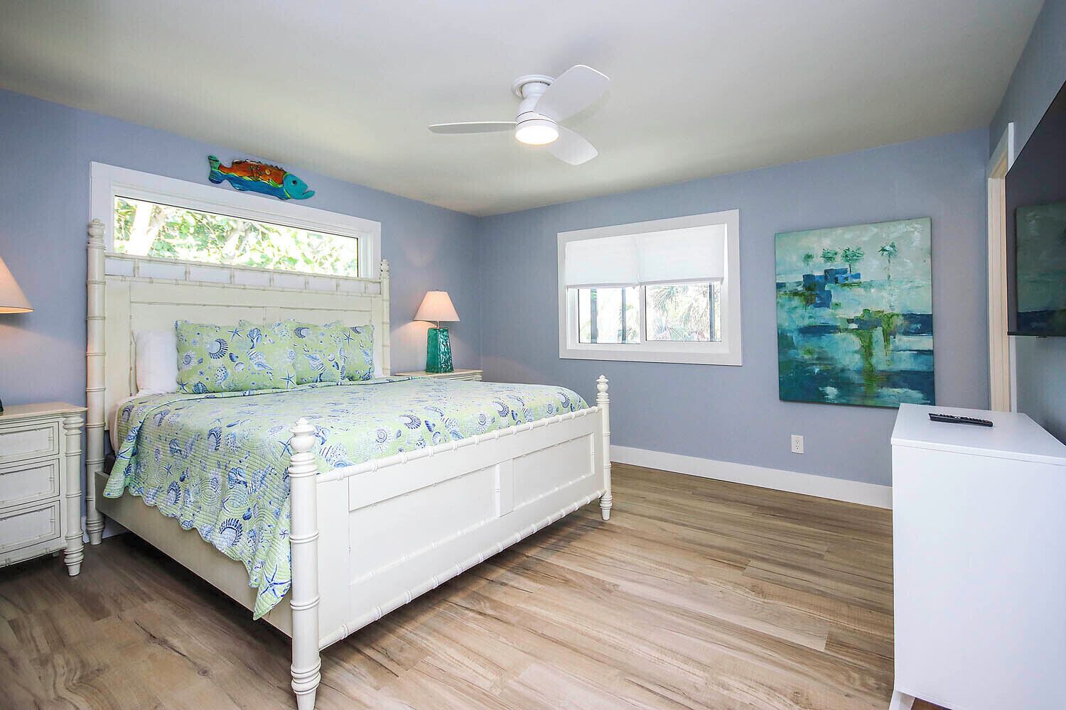 A bedroom with a bed, two bedside tables, a ceiling fan, a window, and a painting on the wall.