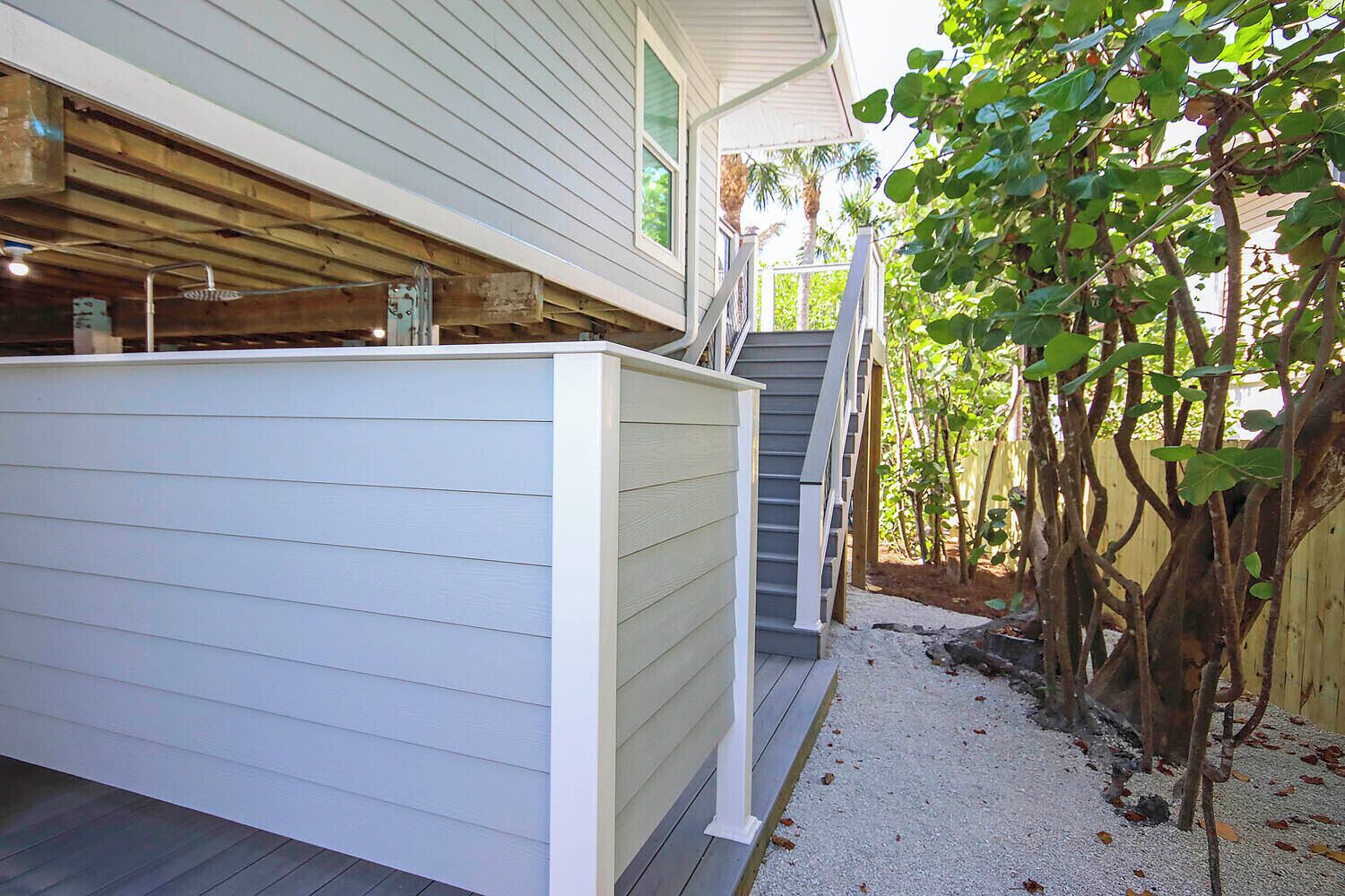 Ein Haus mit überdachter Veranda, einer Treppe zu einem zweiten Stockwerk und einem Garten mit Bäumen und Kies.
