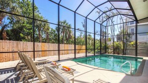 Un área de piscina con terraza de madera, sillas de descanso y un cerramiento de vidrio.