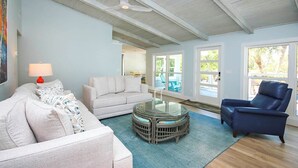 Una sala de estar con un sofá blanco, un sillón azul, una mesa de centro de vidrio y una lámpara roja.