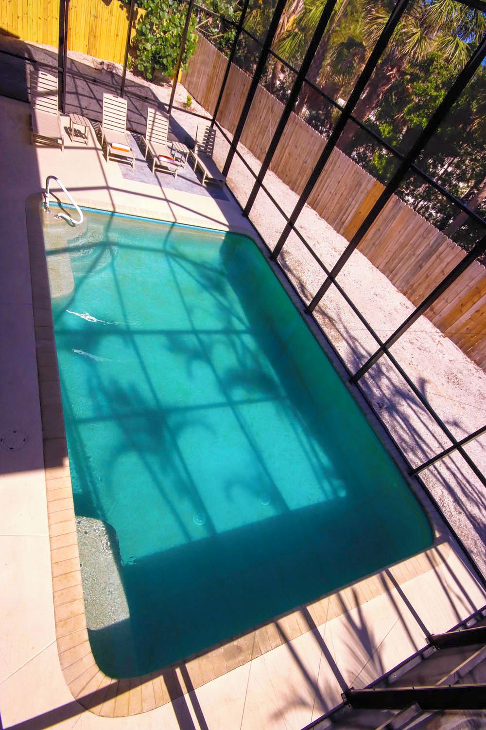 Ein rechteckiger Swimmingpool mit Metallleiter, umgeben von einem Holzzaun und beschattet durch eine Pergola.
