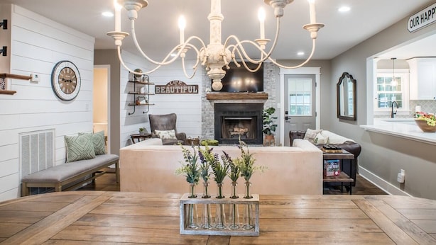 Un salon chaleureux avec une cheminée, un lustre et un coin repas doté d’une table en bois.