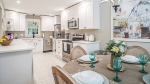 Une cuisine moderne avec des meubles blancs, des appareils en acier inoxydable et un coin repas avec une table mise pour deux personnes.