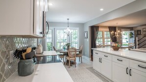 Une cuisine moderne avec des meubles blancs, un îlot central et un coin repas agrémenté d’un lustre.
