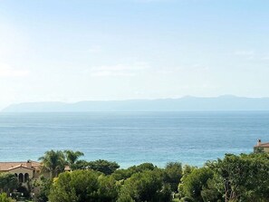 Vista costera con cielo despejado, una masa de agua y una cadena montañosa distante.