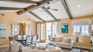 Un salon spacieux avec un plafond haut, un coin repas agrémenté d’un lustre, et une grande fenêtre laissant entrer la lumière naturelle.