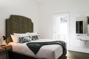 A neatly made bed with white linens and a dark headboard, a bedside lamp, and a nightstand with a lamp.
