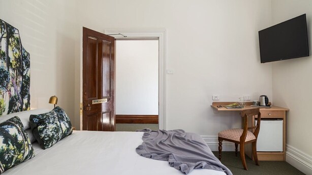 Une chambre d’hôtel comprenant un lit, un bureau avec une chaise, une télévision et une porte donnant sur une autre pièce.